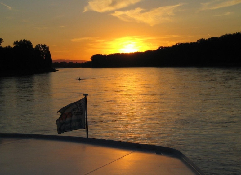 A sunset over a calm river with a boat and a flag in the foreground. 1