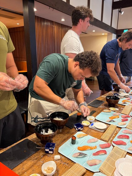 A sushi preparation area with chefs wearing gloves, a wooden table, and various sushi ingredients. 2
