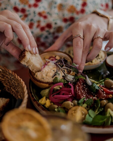 A person serving themselves from a bowl of salad with various vegetables and a creamy dressing. 1
