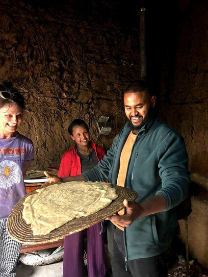 Three people in a cave holding a large flatbread. 4