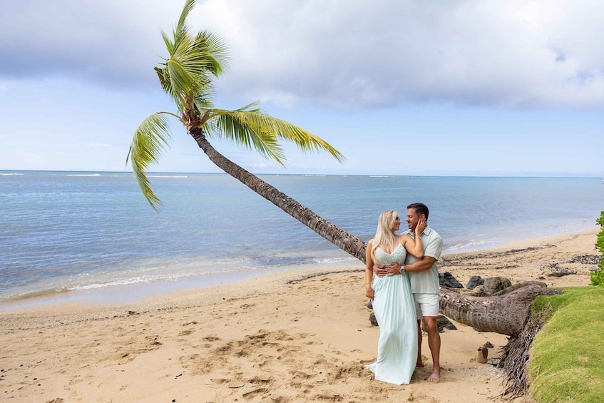 A couple embracing on a beach with a palm tree and ocean in the background. 2