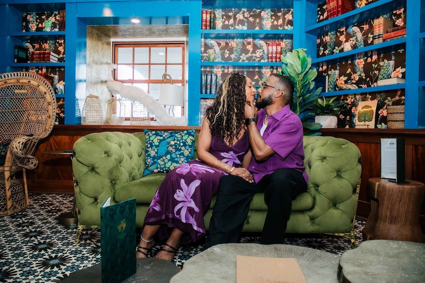 A couple sitting on a green sofa in a room with blue walls, surrounded by bookshelves and decorative items. 5