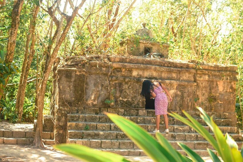 A person standing on stone steps in a forested area with a structure in the background. 2
