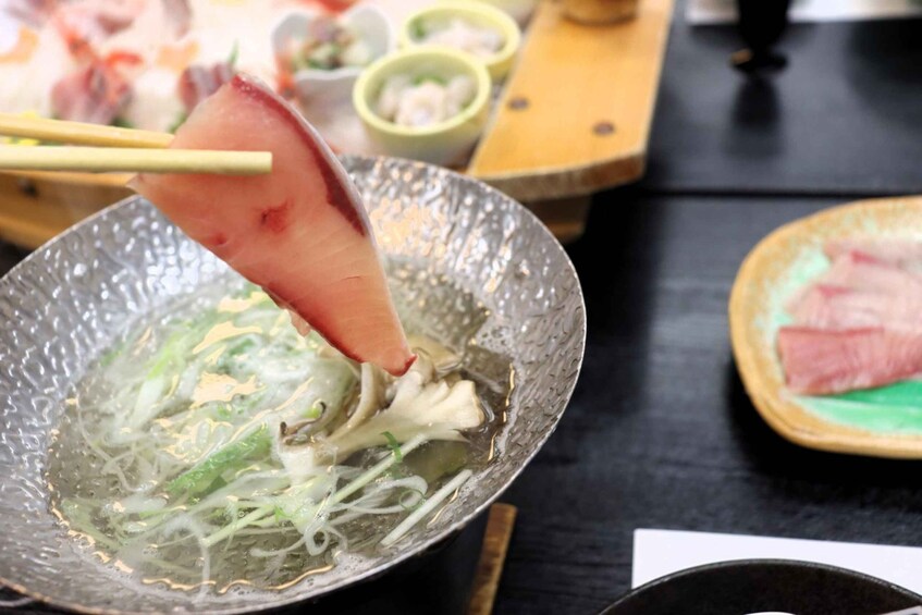 A bowl of clear soup with vegetables and a piece of meat being lifted with chopsticks. 3