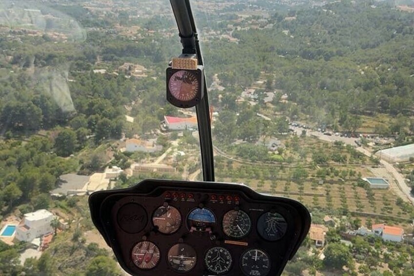 A helicopter cockpit with multiple gauges and a view of a rural landscape with fields and buildings. 3