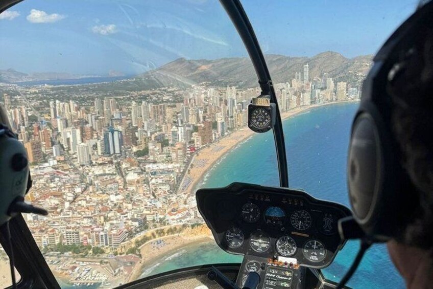 A helicopter cockpit with a view of a coastal cityscape, including a beach and mountains. 5