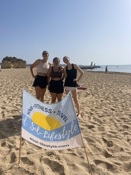 Three people standing on a sandy beach with a flag in front of them. 5
