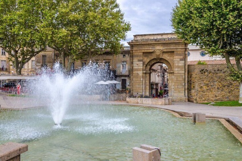 A fountain in a public square with a stone archway and trees in the background. 4