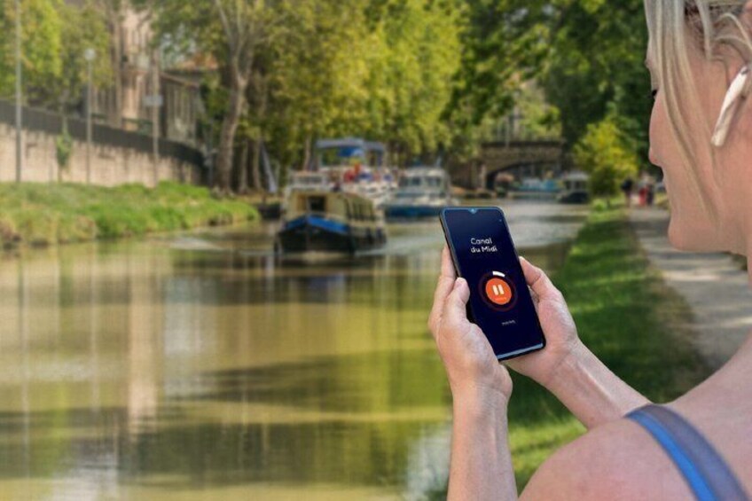 A person holding a smartphone with a canal and boats in the background. 5