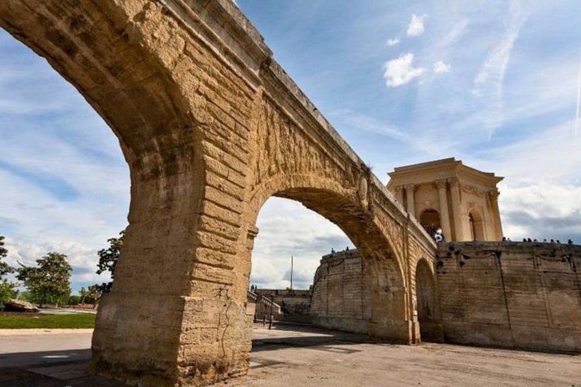 An ancient stone bridge with arches, a round building with columns, and a clear sky. 3