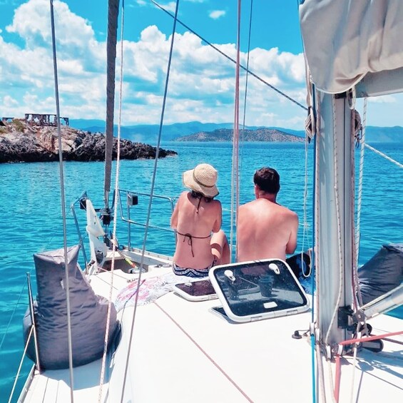 A couple on a sailboat with a rocky coastline in the background. 5