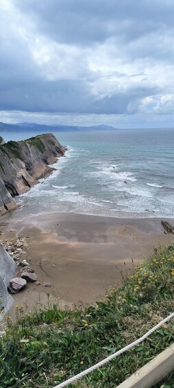 A coastal landscape with a rocky cliff, sandy beach, and a rope barrier. 5