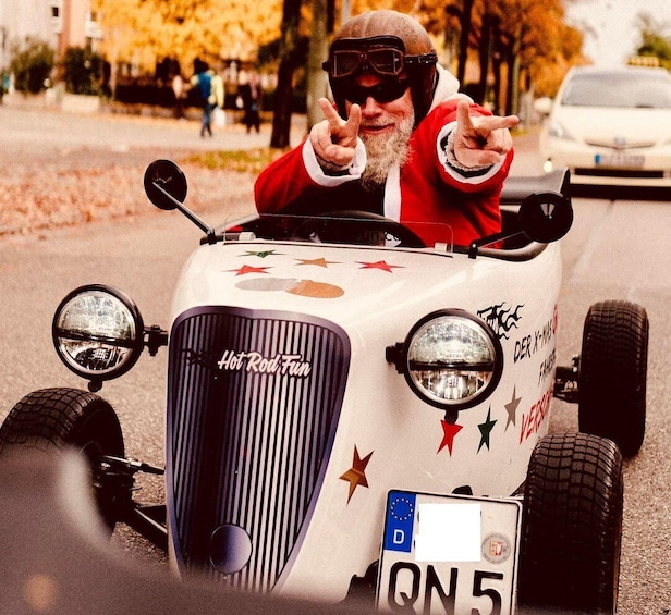 A vintage car with 'Hot Rod Fun' and 'DER X-MAS' decals, driven by a person in a red jacket and sunglasses. 2