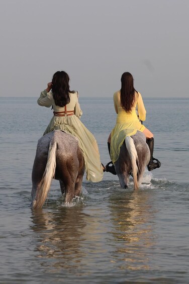 Two women riding horses in shallow water. 2