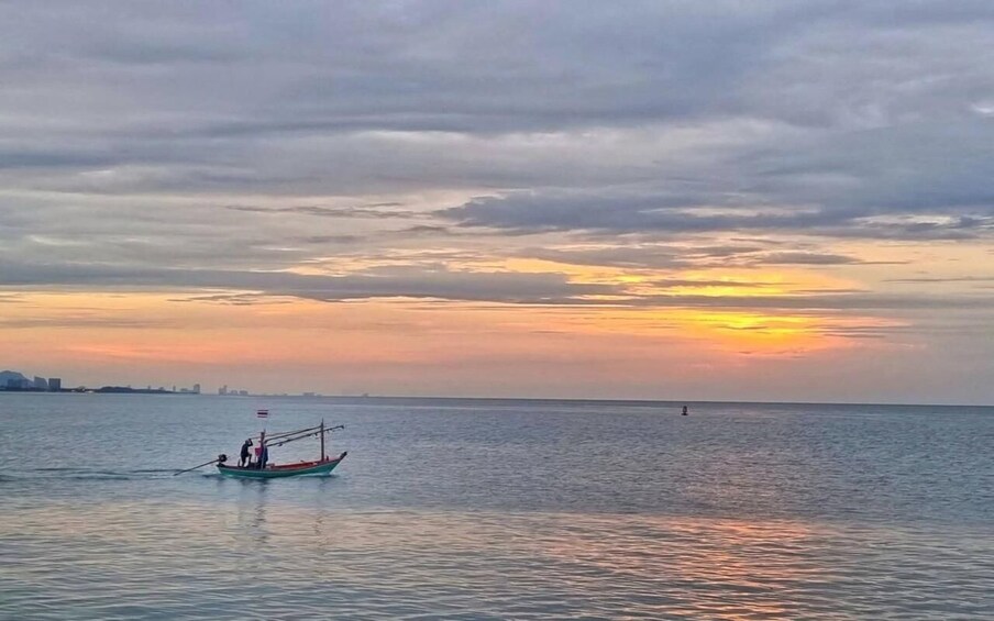 A calm sea at sunset with a boat carrying two people and a flag. 4