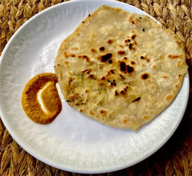 A flatbread on a white plate with a side of sauce. 2