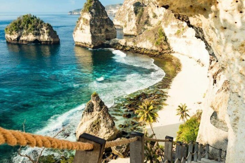 A coastal landscape with clear turquoise waters, white sandy beach, and rocky formations. 1