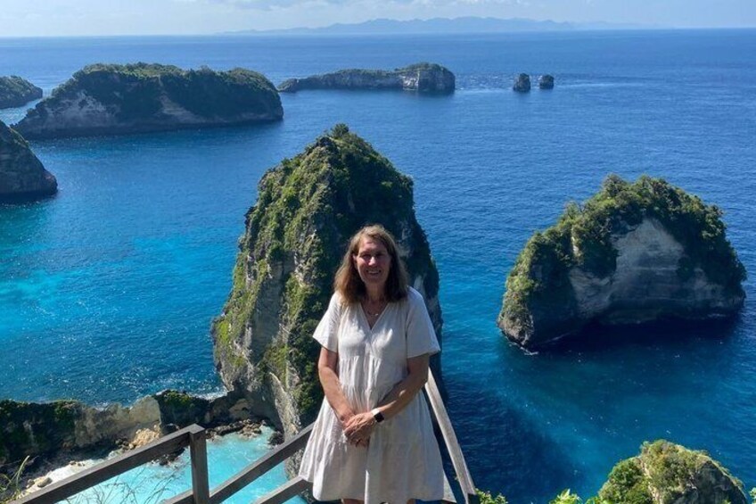A person standing on a wooden staircase overlooking a coastal landscape with clear blue waters and green islands. 5