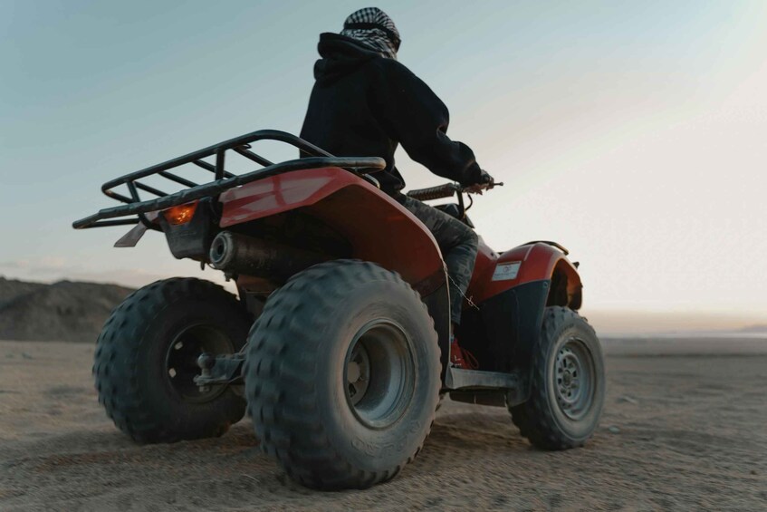 A person riding a red ATV on a sandy terrain. 3