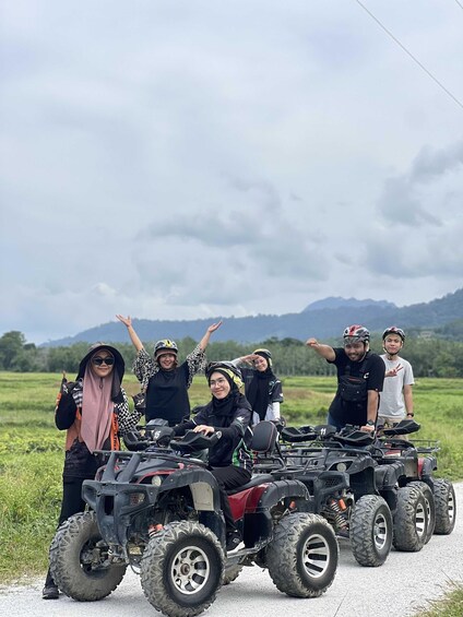 A group of people with ATVs on a rural road with mountains in the background. 1