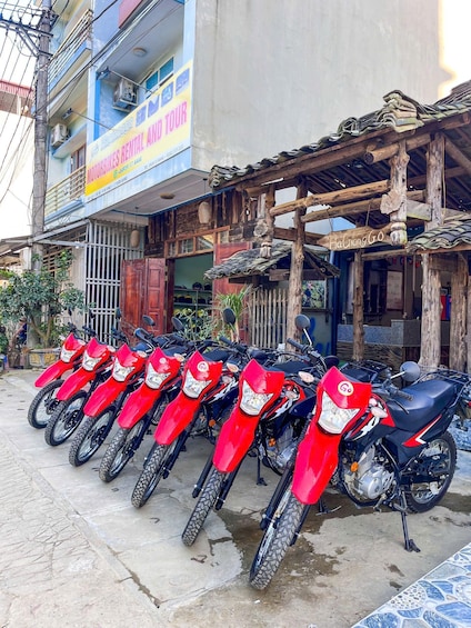 A row of red motorcycles parked outside a building with a sign for 'MOTORBIKES RENTAL AND TOUR.' 4