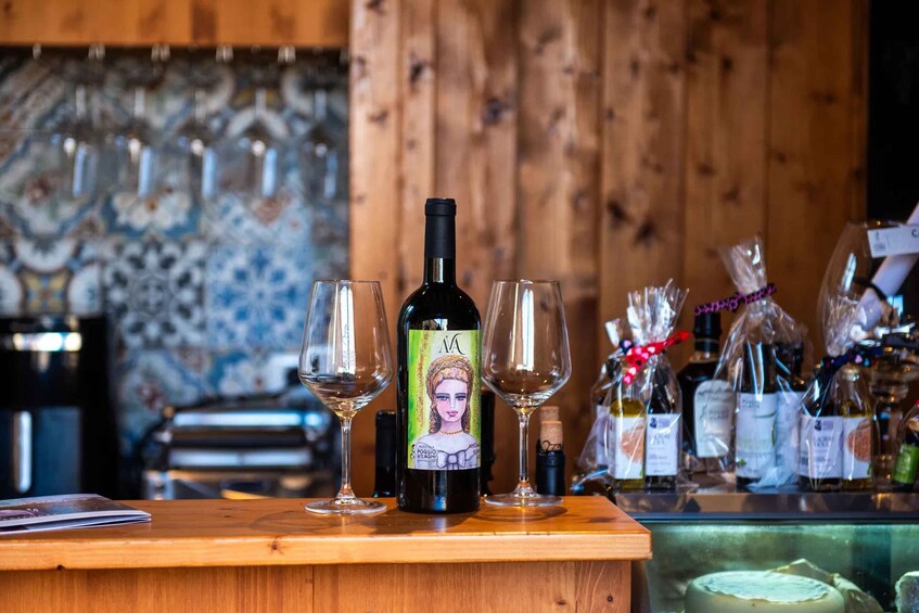 A bottle of wine with a label featuring a woman, two empty wine glasses, and a wooden counter with a tiled backsplash. 3