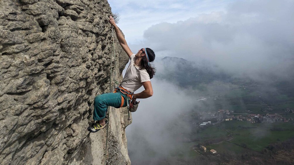 A person rock climbing a steep, rocky cliff with a valley and misty mountains in the background. 3