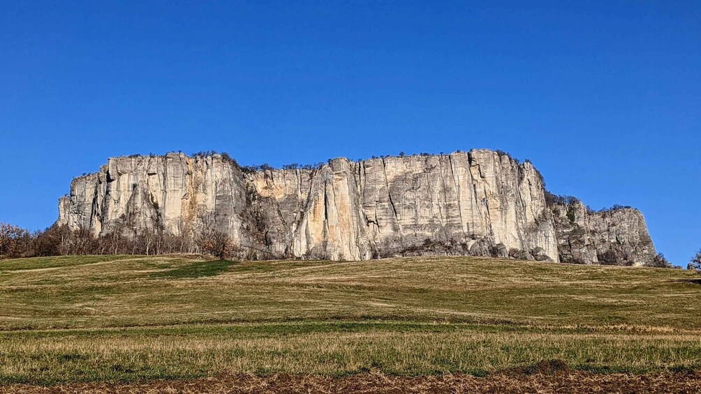 A large limestone cliff with a grassy foreground and a clear blue sky. 4