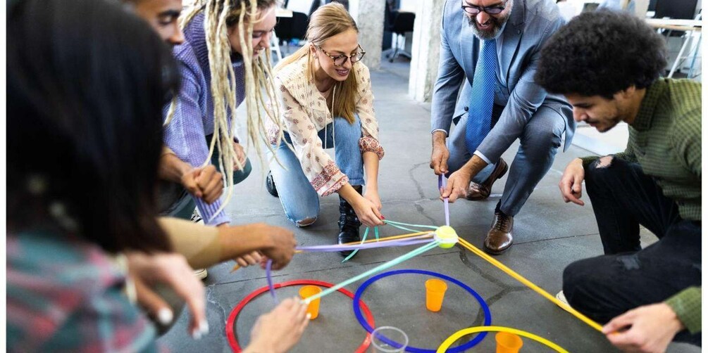A group of people engaged in a collaborative activity involving colorful ropes and cones on a concrete floor. 1