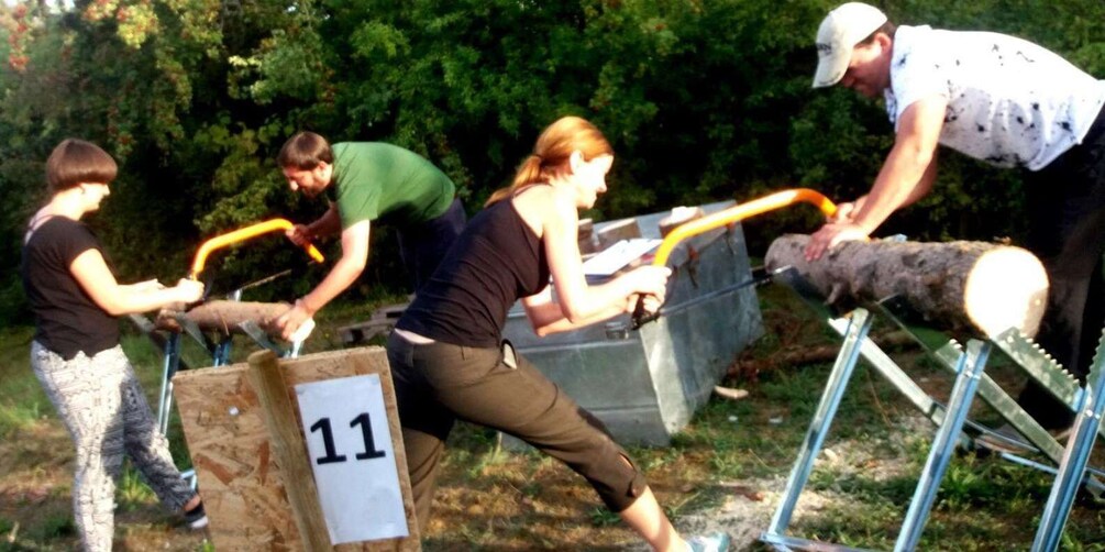 People participating in an outdoor activity, possibly a team-building exercise, with a wooden structure labeled '11' and metal barriers. 5