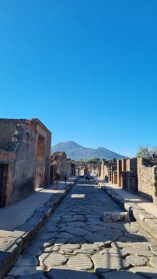 An ancient stone-paved street flanked by ruins, leading towards a mountain. 3