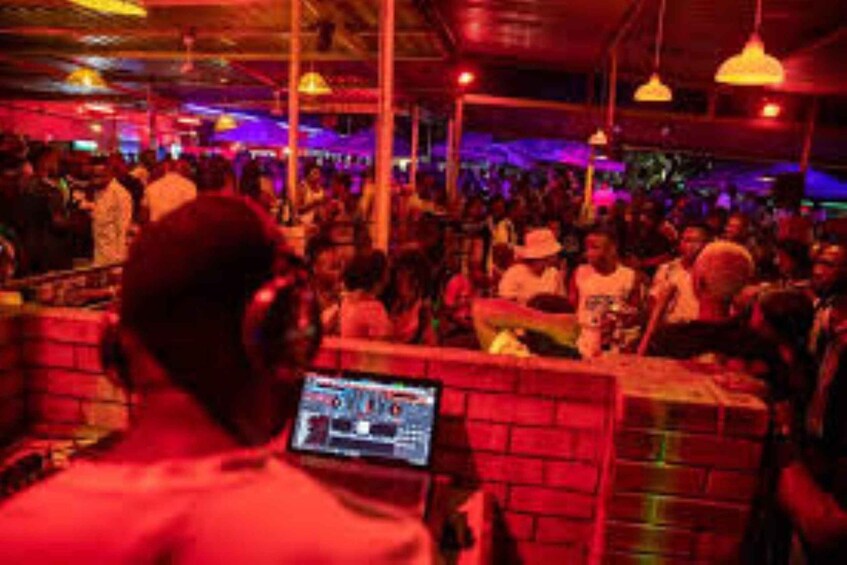 A crowded indoor space with people, a DJ booth, and red lighting. 3