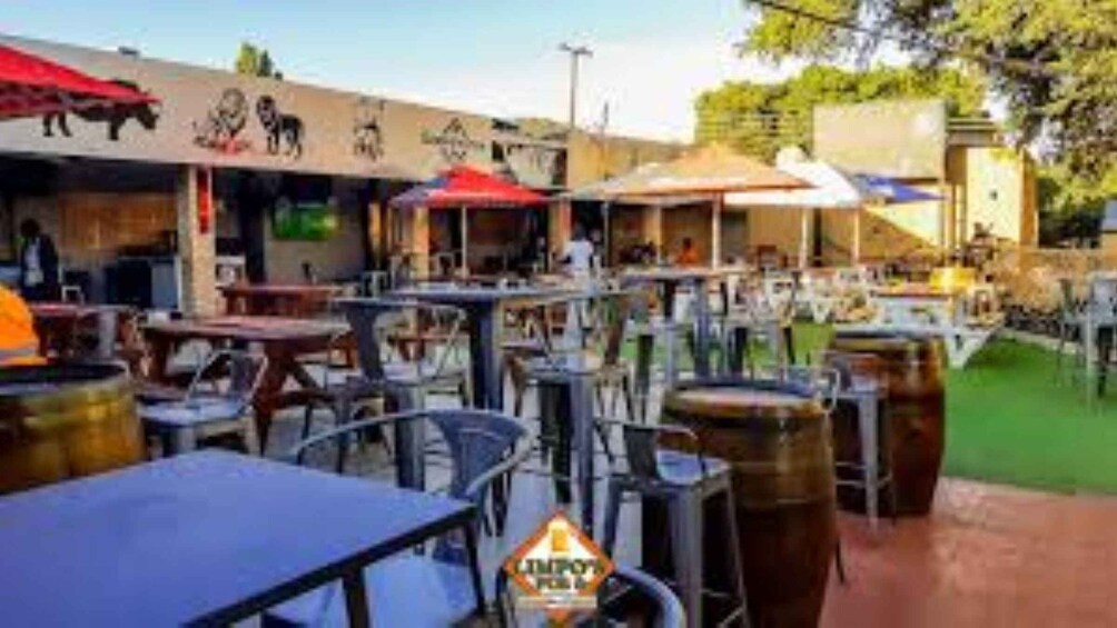 An outdoor dining area with tables and chairs, barrels, and a building with animal murals. 1