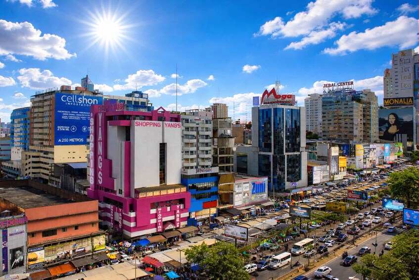 A busy urban street with commercial buildings, including a pink and blue structure with 'Shopping Yang's' signage. 1