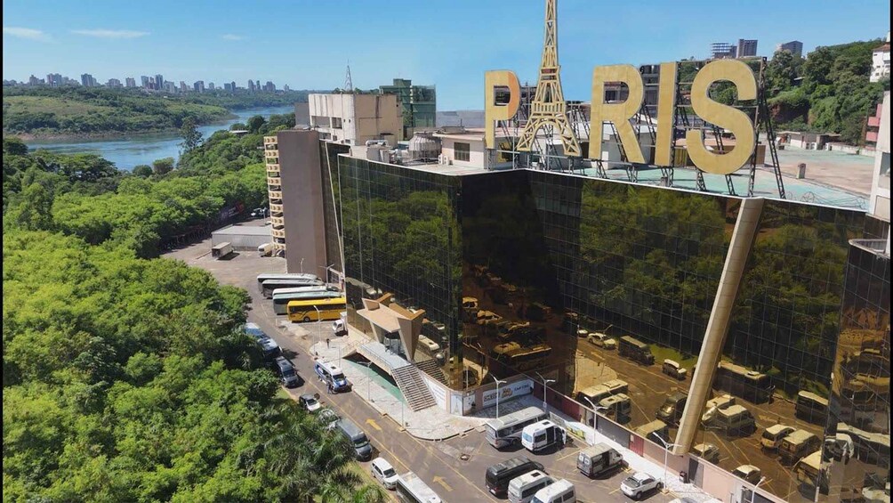 A modern building with a large 'PARIS' sign, surrounded by lush greenery and a river. 3