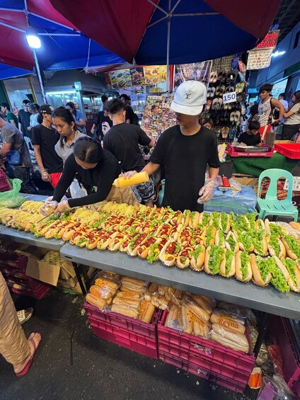 A bustling market with a table of hot dogs and bread. 3