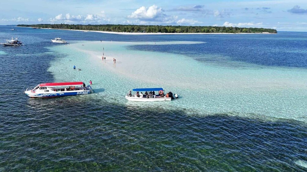 A clear tropical sea with two boats, one labeled 'FUN BOAT,' and a sandy beach with a forested island in the distance. 2