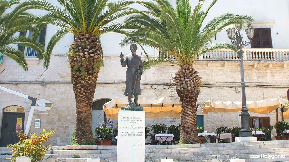 A statue in a square with palm trees and outdoor seating. 1