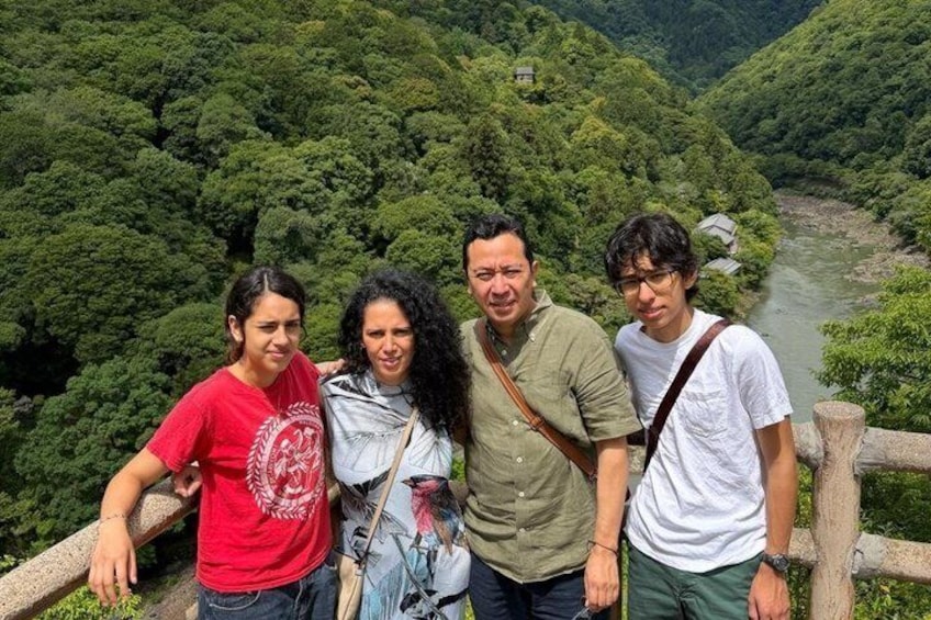 Four people standing on a wooden platform with a river and forested valley in the background. 2