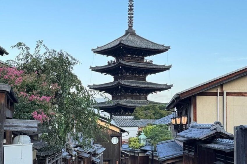 A traditional Japanese pagoda with multiple tiers, surrounded by wooden buildings and blooming pink flowers. 1
