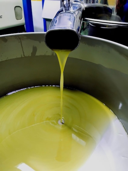 A metallic container with a spout pouring a yellowish liquid into a larger container. 3