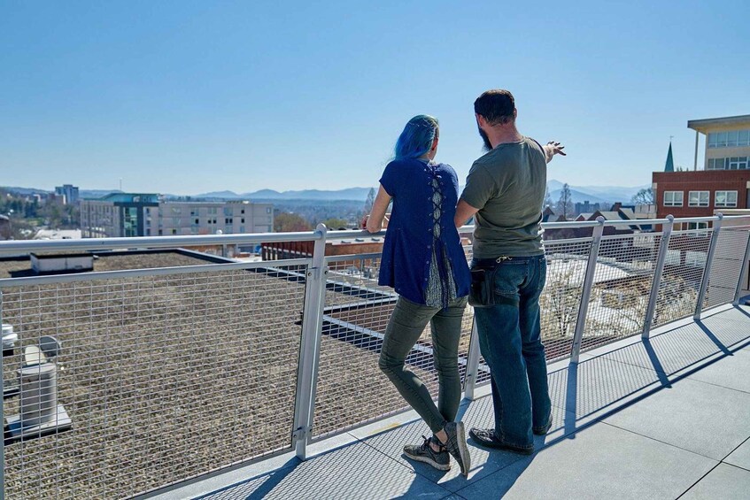 Two people standing on a rooftop with a cityscape in the background. 4