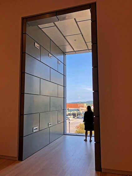 A person standing in a hallway looking out at a street with buildings and a clear sky. 3