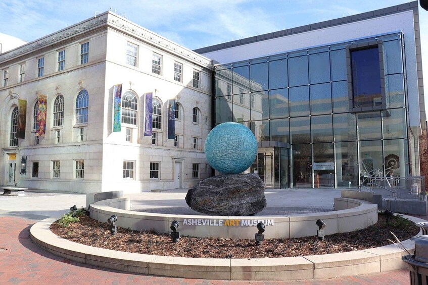 The Asheville Art Museum with a sculpture of a blue sphere on a rock, surrounded by a brick walkway. 5