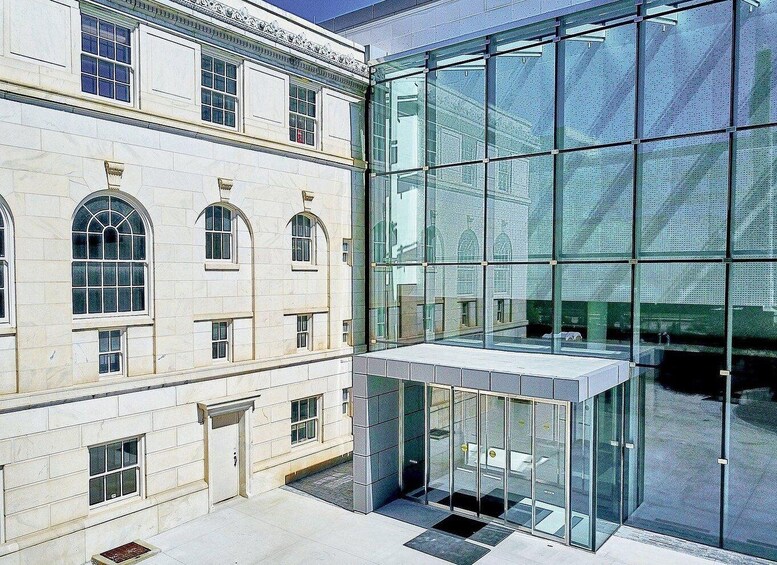 A modern glass building adjacent to a classical building with arched windows. 2