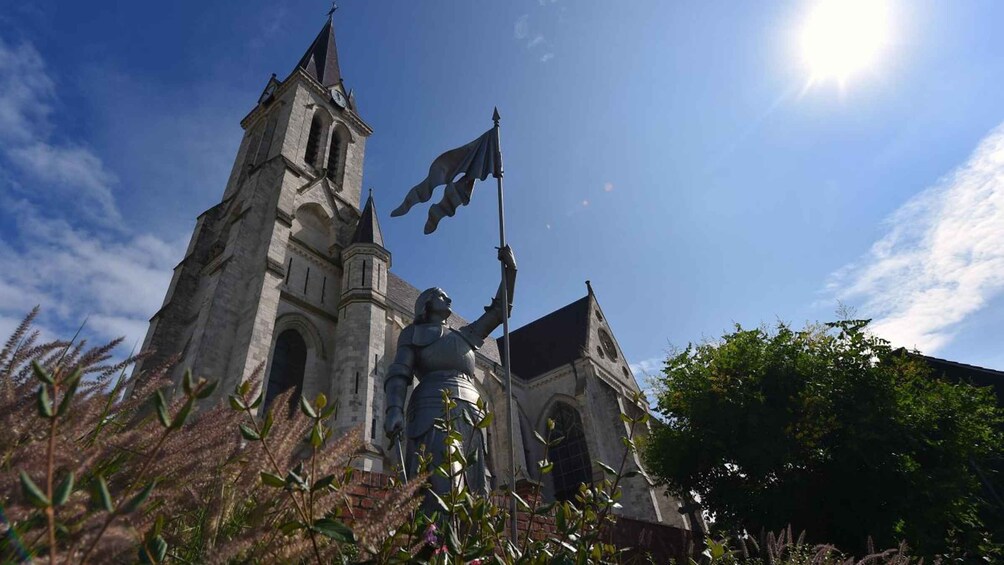 A church with a clock tower and a statue of a knight holding a flag. 1