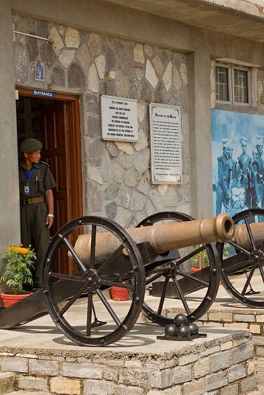 A stone building with a signboard, a large cannon, and a person standing at the entrance. 3