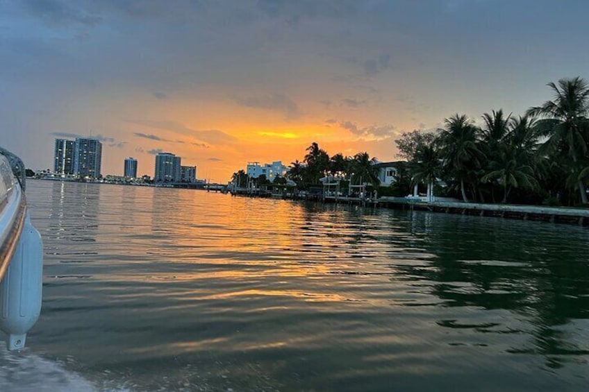A sunset over a body of water with buildings and palm trees in the background. 2