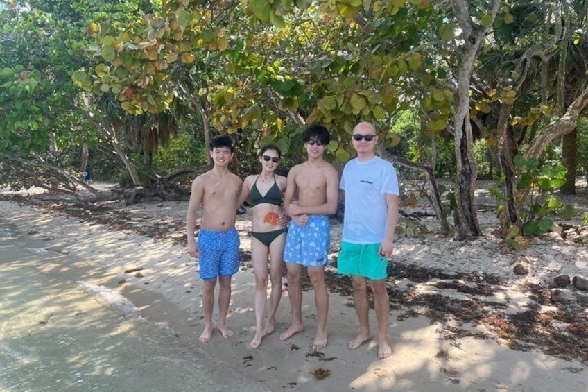 Four people standing on a sandy beach with trees in the background. 4