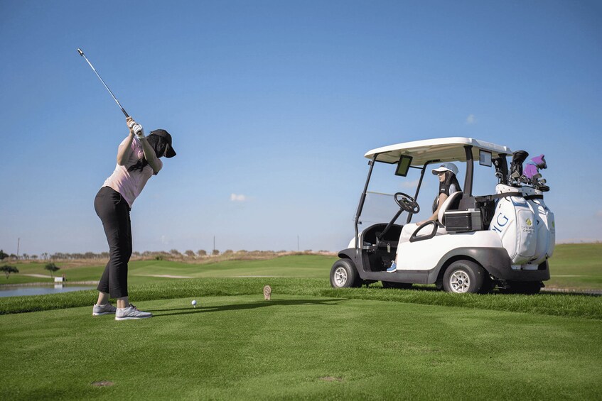 A golfer preparing to hit a ball on a golf course with a golf cart nearby. 4